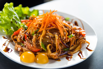 Pasta with sesame and carrot on a plate with salad.