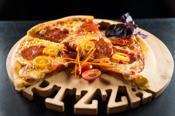Pizza with sausage and tomatoes on a wooden round tray with a carved inscription 