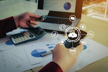 young man entering security code with smart phone and paying with credit card and laptop computer on desk at home office with graphic icon diagram, payment and shopping online, technology concept