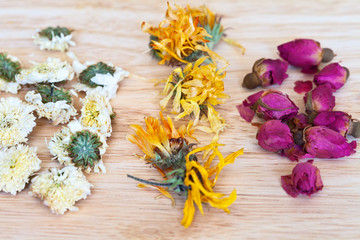 Dried flowers of white chrysanthemum, orange calendula and buds of pink rose for green herbal tea on a wooden table