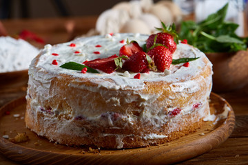 Strawberry tart covered with whipped sour cream on a wooden tray over rustic background, selective focus
