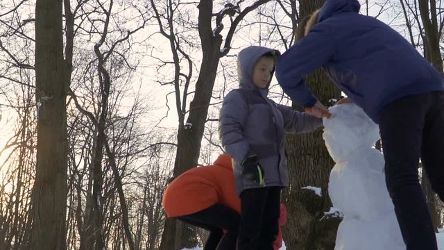 Children make snowman together in winter park