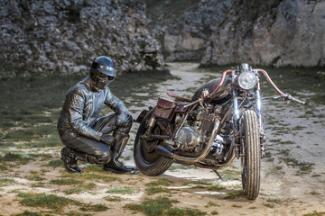 Biker with black leather suit and mask stay on a custom special rat motorbike. Post apocalyptic concept
