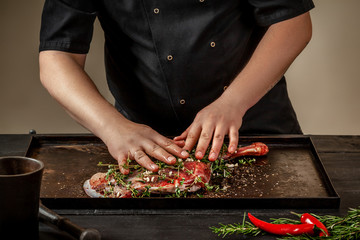 Male chef rubbing raw lamb shanks with greens and spices on stone tray on wooden table. Chef cooking appetizing shank of lamb.