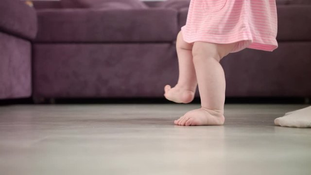 Baby girl doing first steps at home. Child feet walking on floor with father support. Baby learn to walk with daddy. Infant learning walk. Little feet step at home