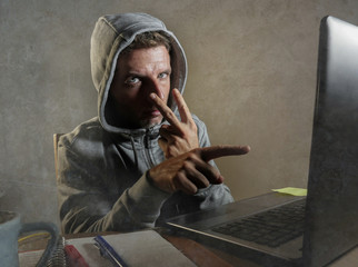 dangerous looking hacker man in hoodie hacking internet computer system pointing his eyes warning...