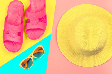 Hat, sunglasses and slippers on a three-color pastel background of blue, yellow and pink.