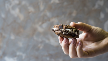 A female hand holds an ice cream sandwich with a chocolate cookie on a gray background. Summer dessert concept