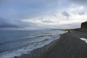 Thunderclouds over the mountain lake; sacred Namtso Lake (Tibet); group of people walk along the shore on a ritual pilgrimage (kora)