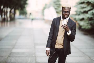 Portrait of a happy young man in suit walking and reading text message on his mobile phone in the...