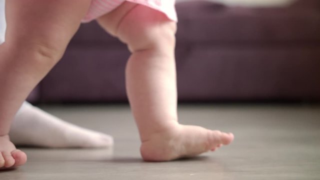 Baby learning walk. Close up of little feet doing first steps at home. Toddler walk on floor. Daddy support child in learning to go. Happy new life concept. Little feet step