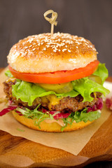 Close up of a american burger with sous, tomatoes, pickles, lettuce,and cheese on wooden table.