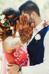Bride reaches out her hand with henna tattoo while groom kisses her