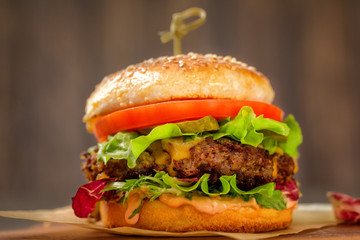 Home made burger with sous, tomatoes, pickles, lettuce,and cheese on wooden table