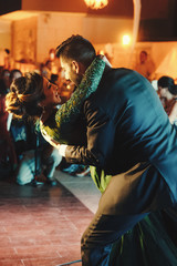 Indian groom in a classy black suit and beautiful bride in a green evening gown dance in the restaurant