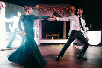 Indian groom in a classy black suit and beautiful bride in a green evening gown dance in the...