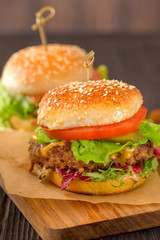 Close up of two american burgers with sous, tomatoes, pickles, lettuce,and cheese on wooden table.