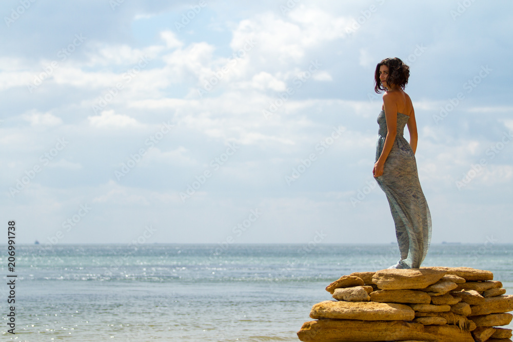 Wall mural beautiful woman standing on the stones with sea and sky backgro