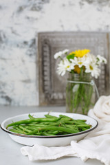 Freshly Picked Green Beans in a White Bowl against a Gray Background; Flowers and Tin Tile faded in Background