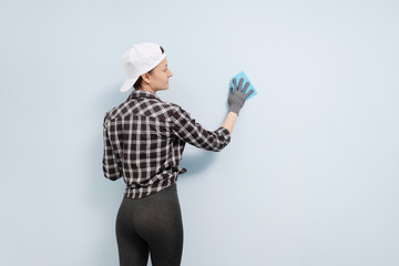Girl painter, designer and worker paints a roller and brush the wall. Smiling, working with pleasure, close-up.