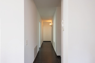 White corridor with only a lit yellow lamp.