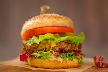 Close up of a american burger with sous, tomatoes, pickles, lettuce,and cheese on wooden table.