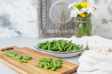 Fototapeta na wymiar Freshly Picked Green Beans in a White Bowl, Some Cut on Cutting Board, all on Gray Background