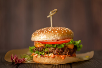 Home made burger with sous, tomatoes, pickles, lettuce,and cheese on wooden table.