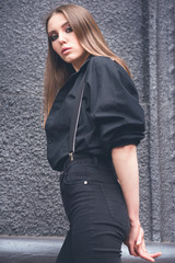 Beautiful girl in black clothes oversize with suspenders. Dark background. Toned image.