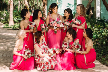 Pretty Indian bridesmaids in red sari stand around beautiful bride in pink sari posing outside