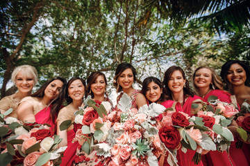 Pretty Indian bridesmaids in red sari stand around beautiful bride in pink sari posing outside