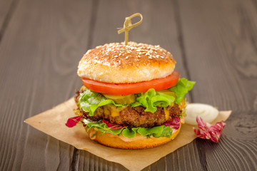Close up of a american burger with sous, tomatoes, pickles, lettuce,and cheese on wooden table.