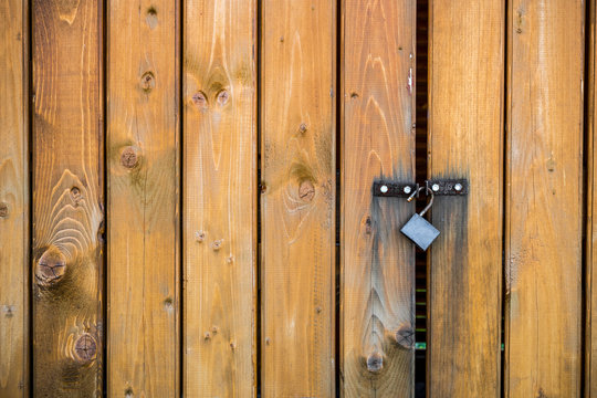 Wooden door made of vertical planks with an open padlock hanging on it