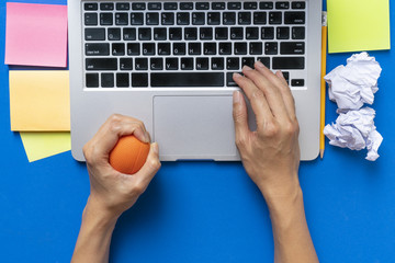 Office worker typing email on computer, feels stressed and nervous, holds a stress ball in her hand