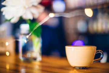 A cup of cappuccino with christmas lights on the bar counter in a cafe