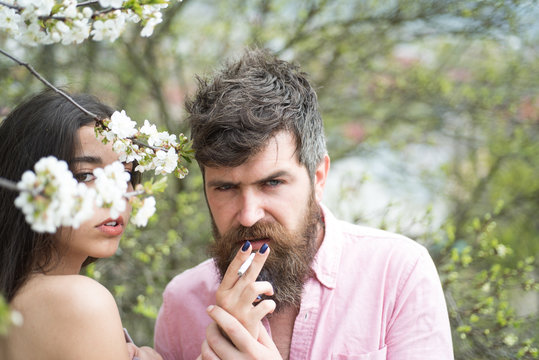 Couple smoking near blooming trees. Couple in love spend time in spring garden, branches with flowers on background. Smoking concept. Female hands holds cigarette for man in garden on spring day.