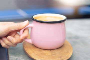 women hand touch pink cup of hot coffee on wooden plate