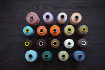 Rows of colourful bobbins with coloured threads on a wooden background