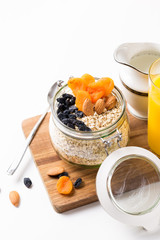 Healthy breakfast in glass mason jar with oat flakes, granola, milk, dry fruits and nuts, dates, honey, orange juice, eggs for morning fitness on wooden board platter on white background isolated