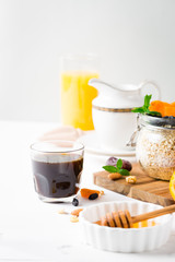 Healthy breakfast in glass mason jar with oat flakes, granola, milk, dry fruits and nuts, dates, honey, orange juice, eggs for morning fitness on wooden board platter on white background isolated