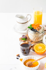 Healthy breakfast in glass mason jar with oat flakes, granola, milk, dry fruits and nuts, dates, honey, orange juice, eggs for morning fitness on wooden board platter on white background isolated