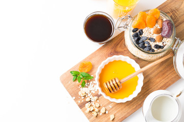 Healthy breakfast in glass mason jar with oat flakes, granola, milk, dry fruits and nuts, dates, honey, orange juice, eggs for morning fitness on wooden board platter on white background isolated