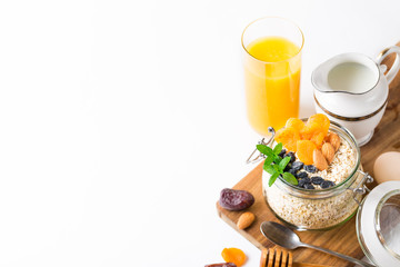 Healthy breakfast in glass mason jar with oat flakes, granola, milk, dry fruits and nuts, dates, honey, orange juice, eggs for morning fitness on wooden board platter on white background isolated