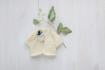 Knitted handmade doll's jacket with a small brooch on a wooden white background