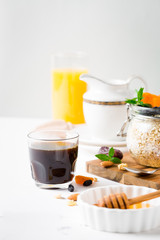 Healthy breakfast in glass mason jar with oat flakes, granola, milk, dry fruits and nuts, dates, honey, orange juice, eggs for morning fitness on wooden board platter on white background isolated