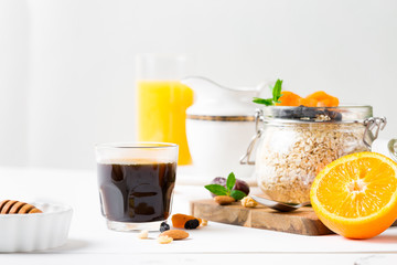 Healthy breakfast in glass mason jar with oat flakes, granola, milk, dry fruits and nuts, dates, honey, orange juice, eggs for morning fitness on wooden board platter on white background isolated