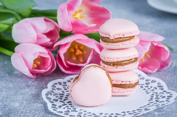 Fototapeta na wymiar Strawberry macarons with pink tulips on blue texture background. Heart shaped. French delicate dessert. Copy space, selective focus. Spring concept.
