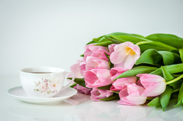 Fototapeta na wymiar Bouquet of tulips and cup of tea on white background. Holiday card. Soft focus, copy space. Spring concept.