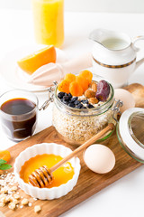 Healthy breakfast in glass mason jar with oat flakes, granola, milk, dry fruits and nuts, dates, honey, orange juice, eggs for morning fitness on wooden board platter on white background isolated