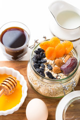 Healthy breakfast in glass mason jar with oat flakes, granola, milk, dry fruits and nuts, dates, honey, orange juice, eggs for morning fitness on wooden board platter on white background isolated